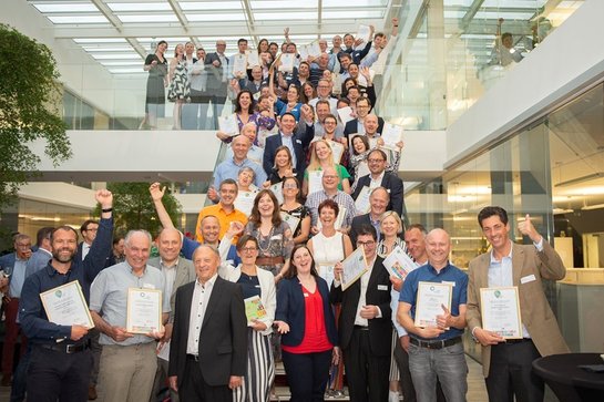 Alle duurzame winnaars op de foto Groepsfoto van lachende mensen op de trap. Alle mensen hebben een charter duurzaam ondernemen vast en lachen of zwaaien naar de camera