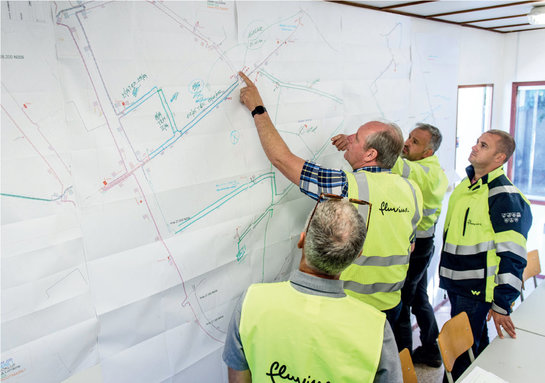 Medewerkers van Fluvius bekijken een plan aan de muur