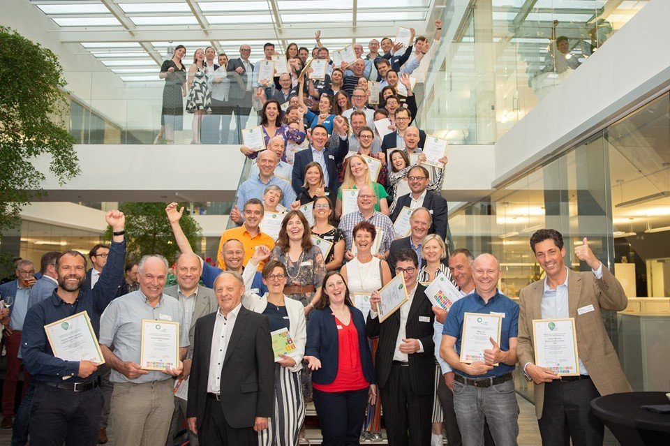 Alle duurzame winnaars op de foto Groepsfoto van lachende mensen op de trap. Alle mensen hebben een charter duurzaam ondernemen vast en lachen of zwaaien naar de camera